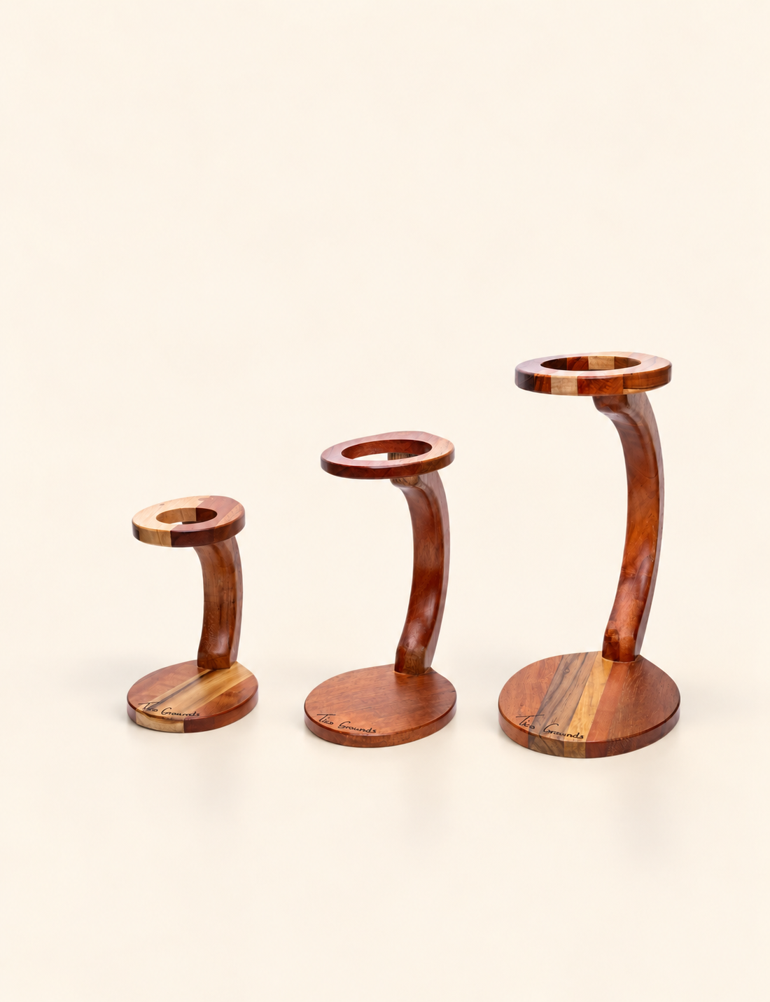 Three curved wooden candlesticks in graduated sizes, arranged from smallest to largest on a plain off-white background.